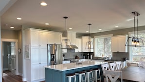 Una cocina moderna con armarios blancos, una isla central con taburetes altos e iluminación colgante.