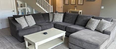 A living room with a sectional sofa, a coffee table, and a staircase.