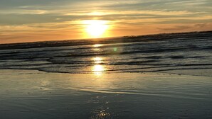 Una playa al atardecer, con el sol reflejado en la arena mojada.
