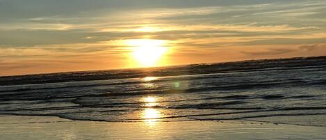 Een strand bij zonsondergang, met de zon die weerkaatst op het natte zand.