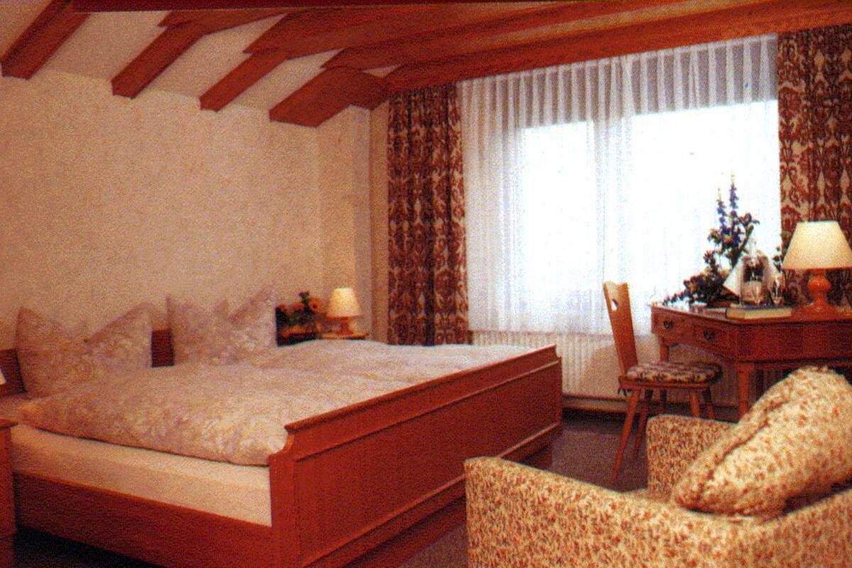 A bedroom with a large bed, a chair, a desk, and a lamp.