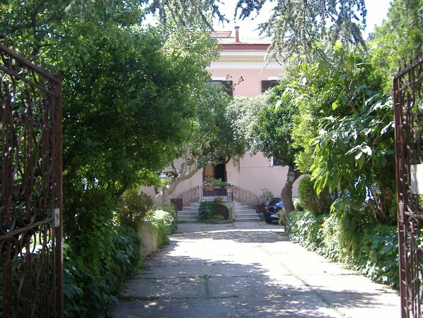 A narrow, tree-lined street leading to a building with a red roof and a staircase. - Lady Ida (Vietri sul Mare)