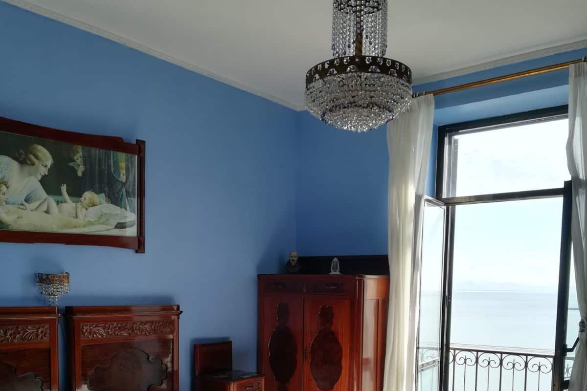 A bedroom with a large bed, a wooden wardrobe, a chandelier, a painting, and a balcony with a view.