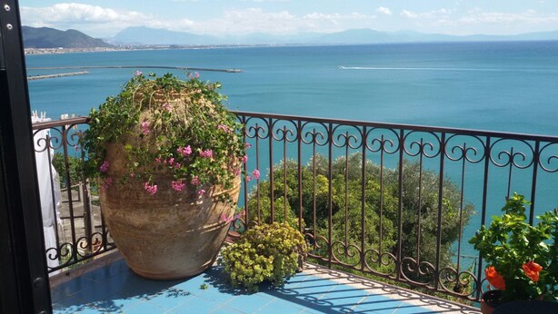 A balcony with a large potted plant, a metal railing, and a view of the sea and mountains. - Lady Ida (Vietri sul Mare)
