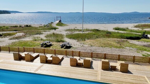 A wooden deck with picnic tables and a swimming pool. - Gullviks Havsbad (Domsjö)