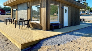 A wooden cabin with a deck, large windows, and a door. - Gullviks Havsbad (Domsjö)