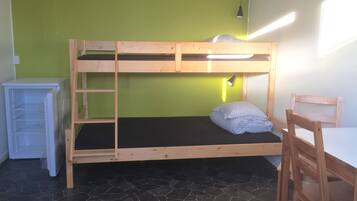 En køjeseng med skrivebord og stol, et lille skab og en lampe monteret på væggen.