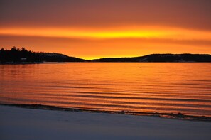 Un atardecer sobre una superficie de agua tranquila con una costa lejana.