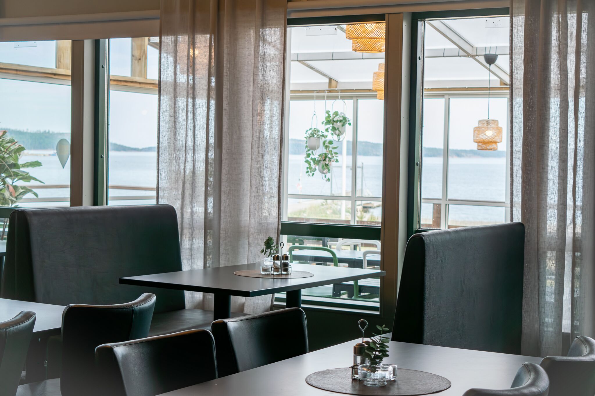 Ein Restaurant mit Seeblick, ausgestattet mit einem Tisch, einer Tischdecke, Stühlen und einer hängenden Pflanze.