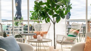 A modern outdoor seating area with wicker chairs and a small round table, surrounded by large windows offering a view of the city. - Gullviks Havsbad (Domsjö)