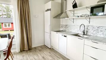 Una cocina compacta con armarios blancos, microondas integrado y salpicadero de mármol.