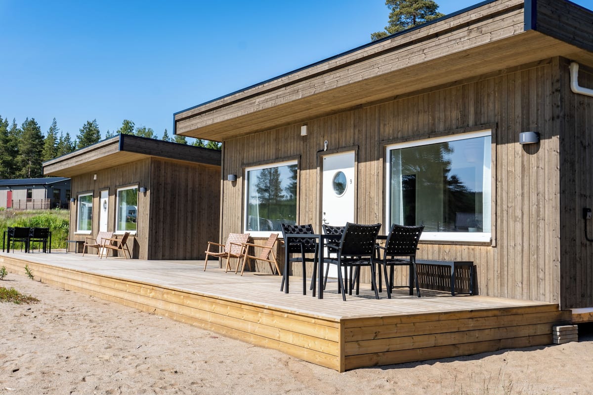 Eine Holzhütte mit großen Fenstern, einer Terrasse und Sitzgelegenheiten im Freien.
