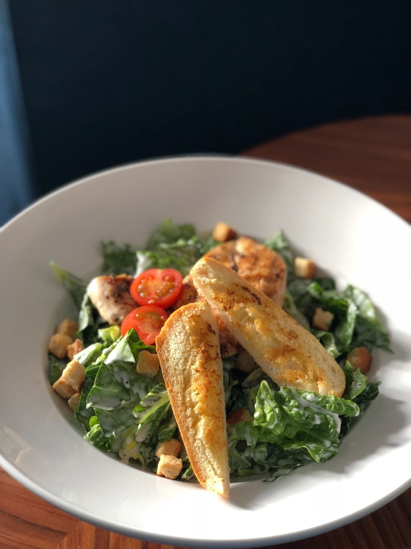 A bowl of salad with grilled chicken, cherry tomatoes, croutons, and toasted bread.