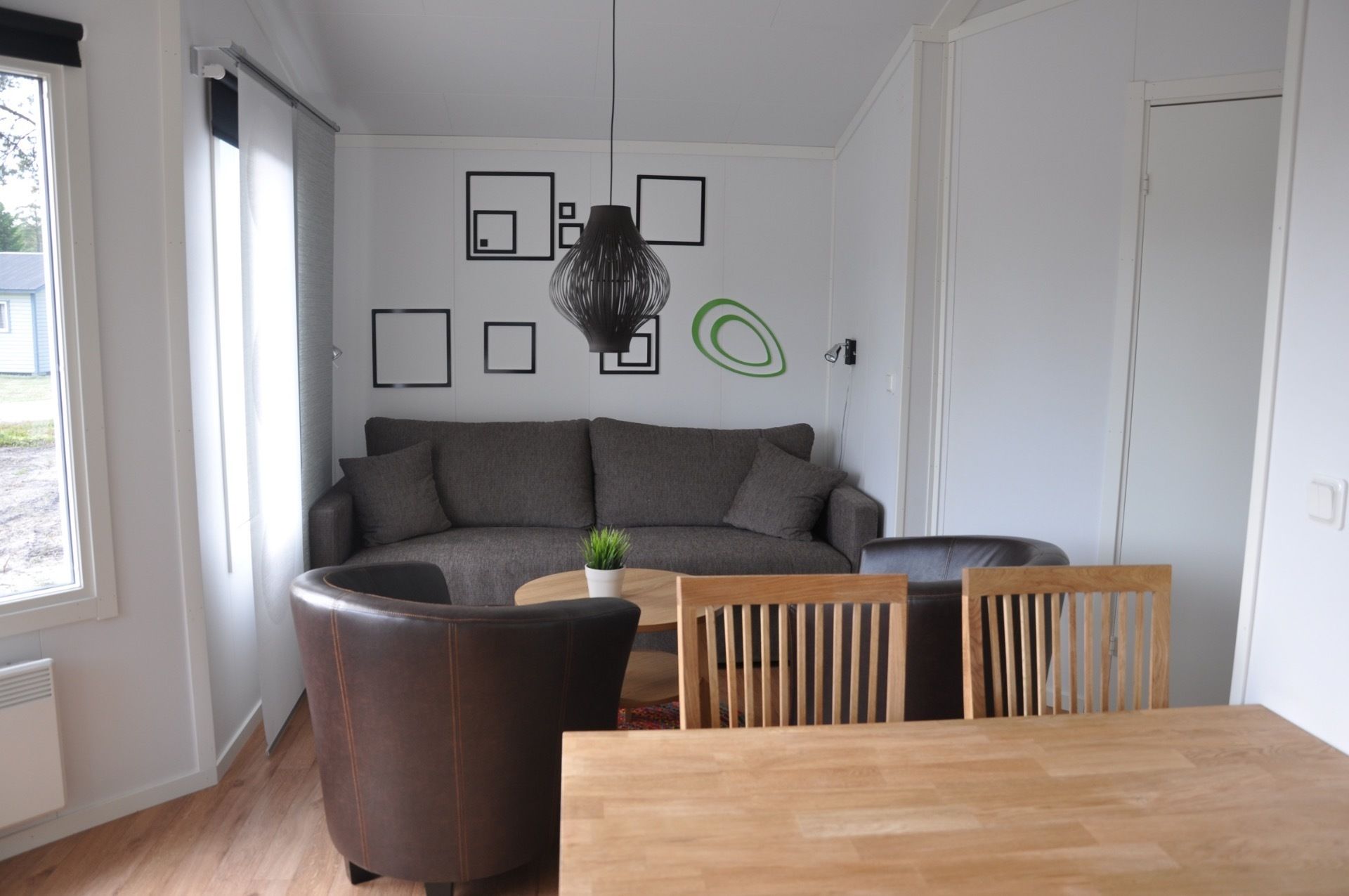 A modern living room with a grey sofa, a wooden dining table, and a black leather armchair.
