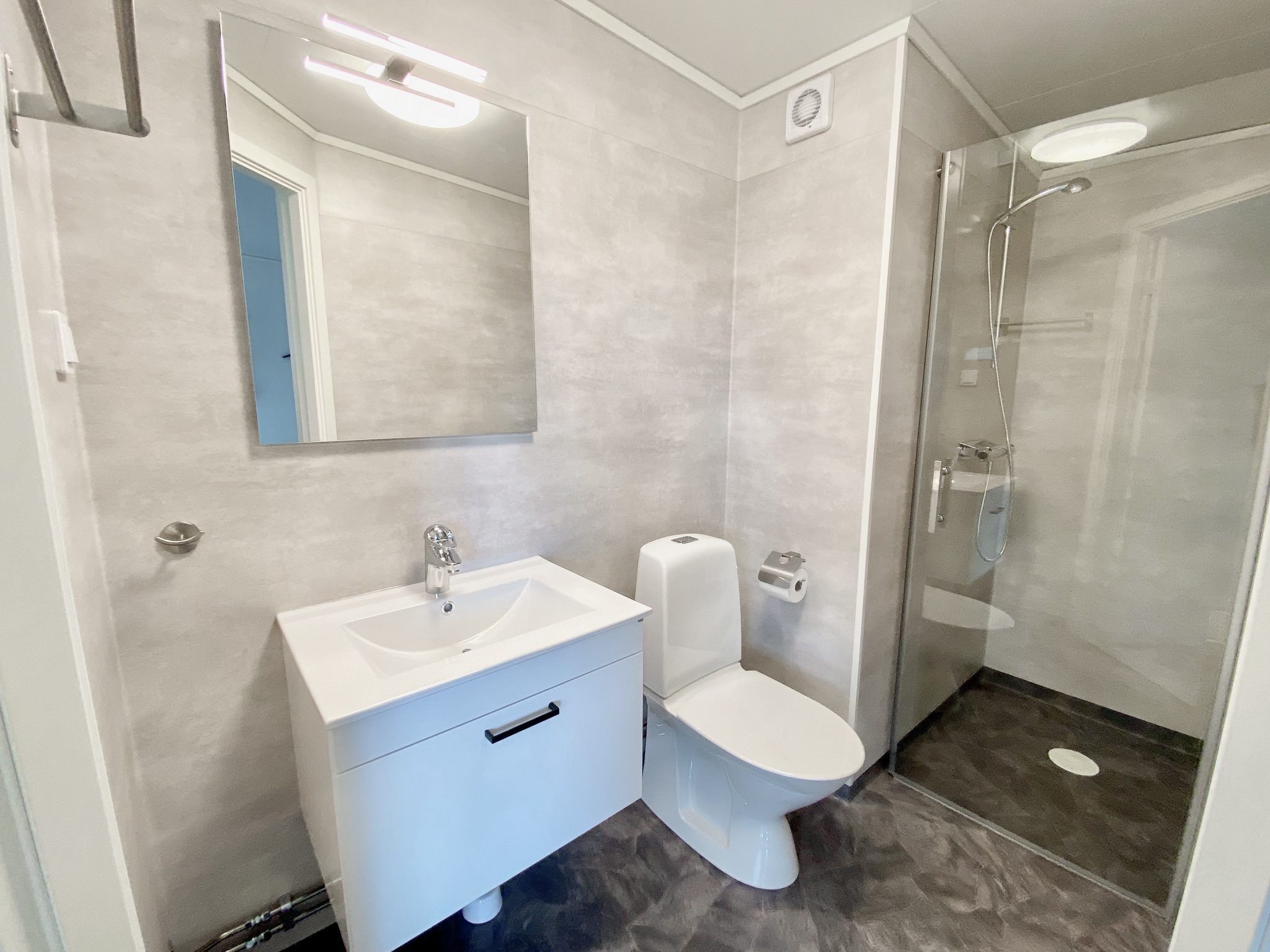 Un baño moderno con un tocador blanco, un inodoro y una ducha con cerramiento de vidrio.
