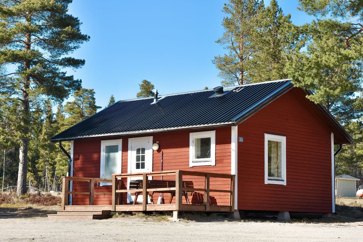 Eine rote Holzhütte mit einer Holzterrasse, umgeben von Bäumen.