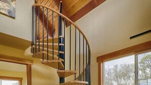Un interior moderno con una escalera espiral, un comedor con una mesa y sillas de madera, y una zona de estar acogedora.