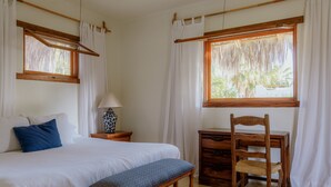 Een slaapkamer met een bed, een bureau, een stoel en een raam met gordijnen.