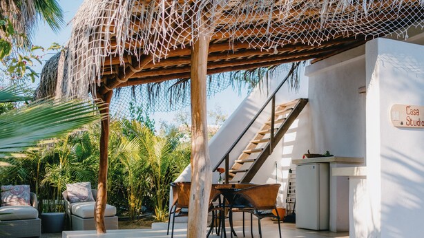 Een overdekt terras met een hangmat, lounge stoelen en een trap naar een hoger niveau.