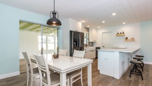 A modern kitchen with white cabinetry, a central island, and a dining area with a white table and chairs. - Sunshine Stay, Central Fort Myers Gated Yard (Fort Myers)