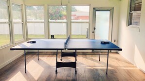 A ping pong table in a room with large windows, wooden flooring, and a ceiling fan. - Sunshine Stay, Central Fort Myers Gated Yard (Fort Myers)