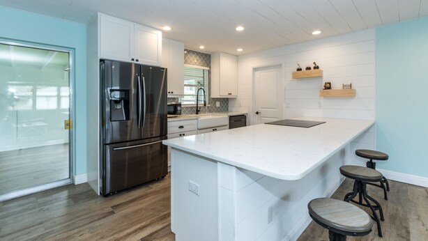 A modern kitchen with white cabinetry, stainless steel appliances, and a large island with bar stools. - Sunshine Stay, Central Fort Myers Gated Yard (Fort Myers)