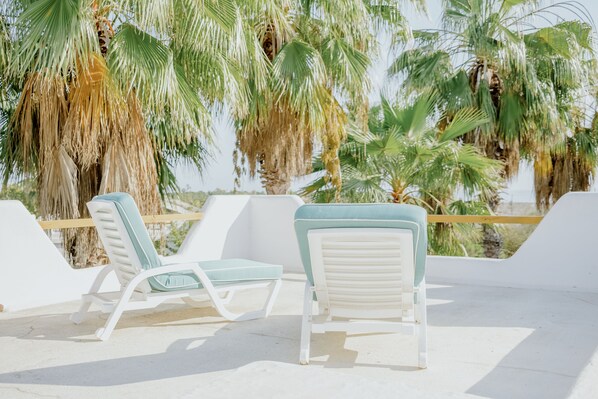 A beachside lounge with white lounge chairs and a view of palm trees.