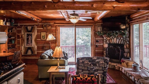 A cozy cabin interior with a fireplace, wooden walls, a dining area, and a large window. - Rustic and Charming one Bedroom cabin. Upgraded pontoon! (Hayward)