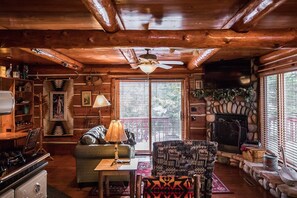 Un intérieur de chalet chaleureux avec une cheminée, des murs en bois, un coin repas et une grande fenêtre.