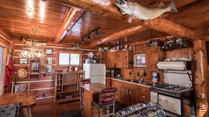 A rustic cabin interior with a wooden dining table, a patterned armchair, a vintage stove, and a mounted fish. - Rustic and Charming one Bedroom cabin. Upgraded pontoon! (Hayward)