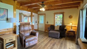 L’intérieur chaleureux d’un chalet avec un plafond en bois, un fauteuil en cuir, un canapé et une table à manger.