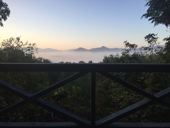Une balustrade en bois offrant une vue sur les montagnes et la brume au loin.