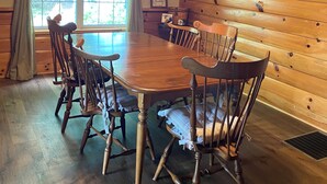 Une table à manger en bois, avec six chaises, un lustre et une fenêtre avec des rideaux.