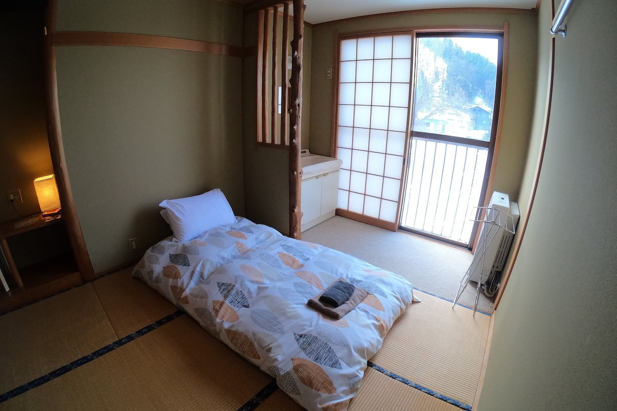 A traditional Japanese-style room with tatami flooring, a futon bed, sliding shoji doors, and a view of a mountainous landscape.