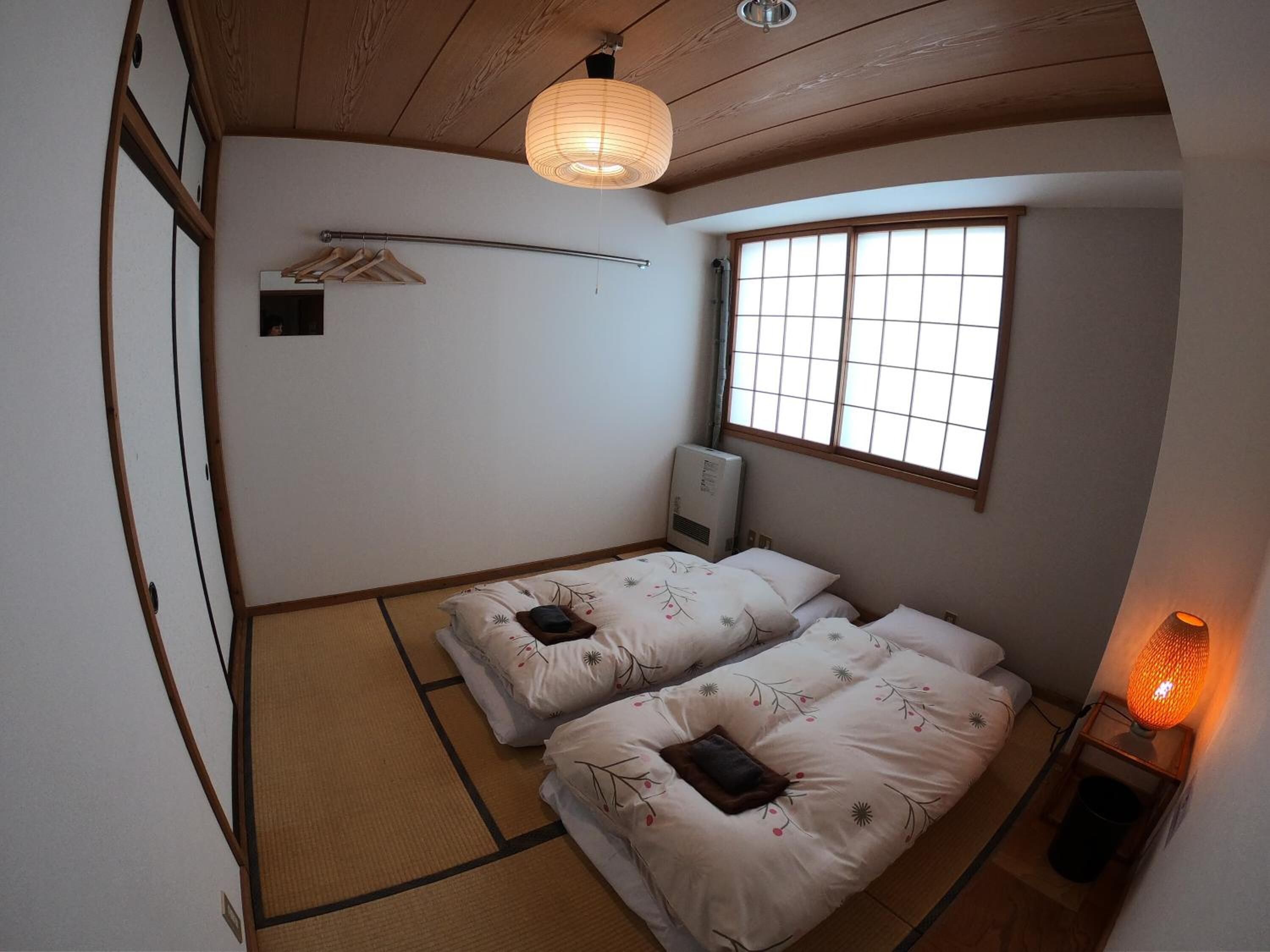 A traditional Japanese-style room with tatami flooring, two beds with floral bedding, a shoji screen, a ceiling fan, and a window with a view.