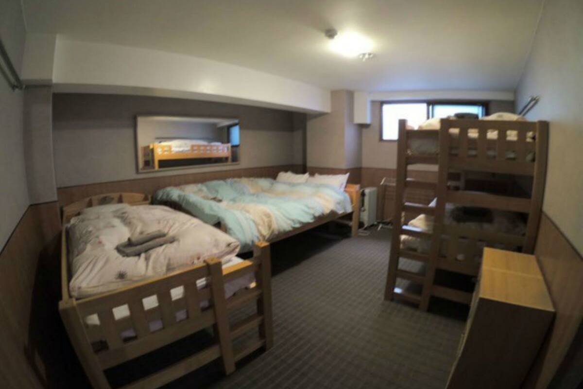A dormitory room with bunk beds, a small desk, and a window providing natural light.