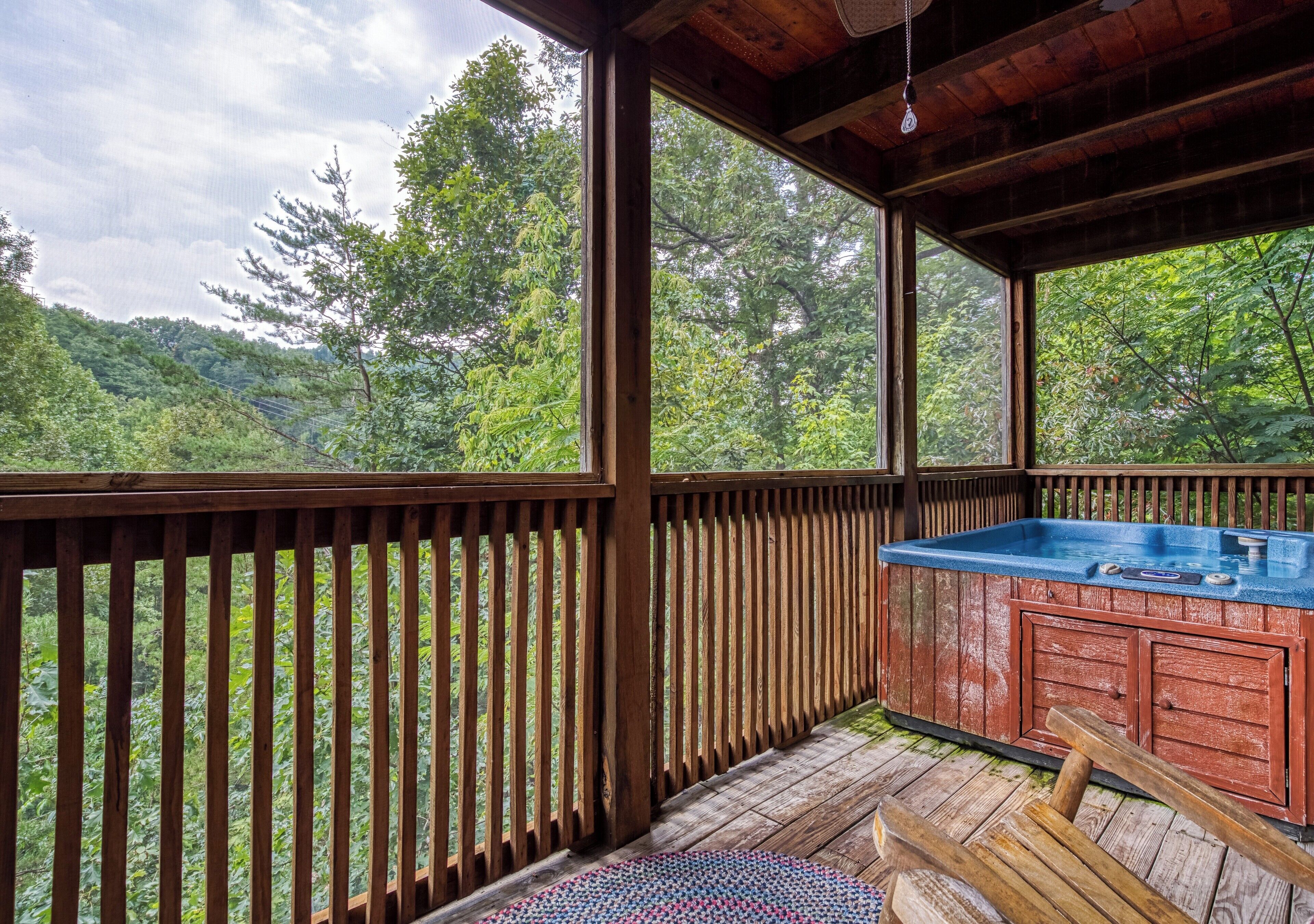 Una terraza de madera con un jacuzzi y vistas a un área boscosa.