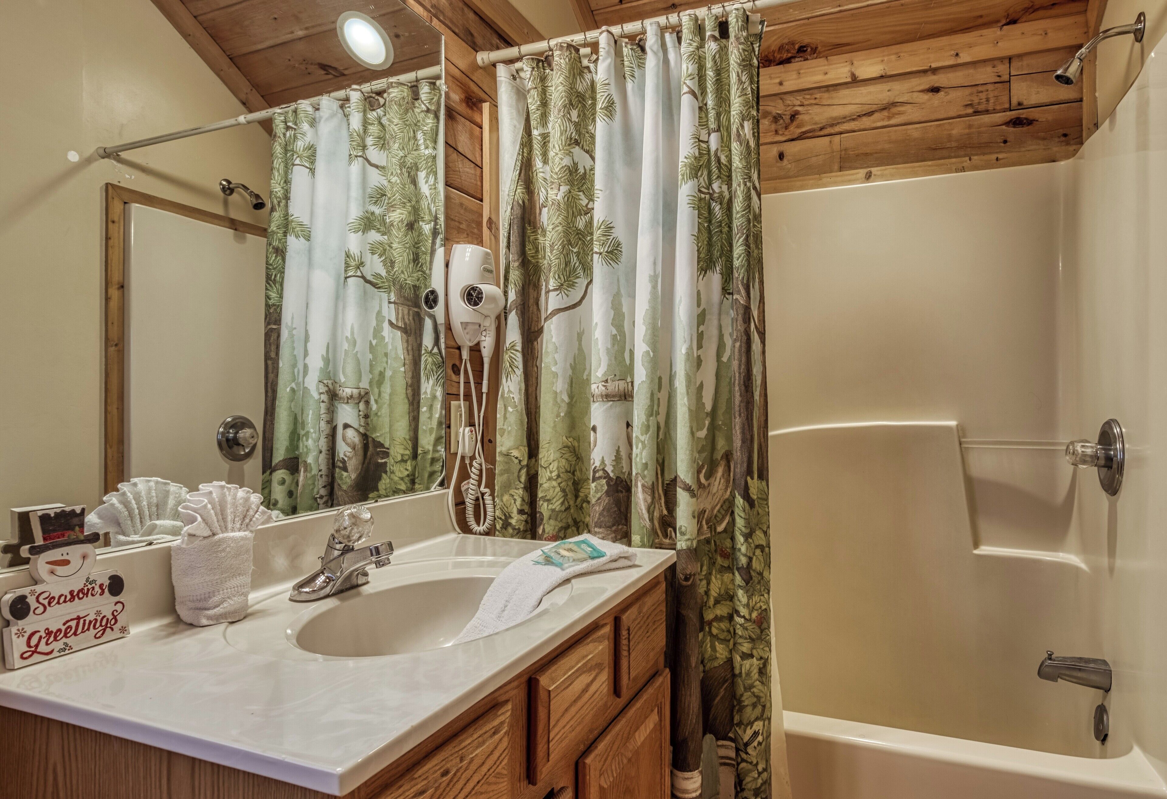 A bathroom with a wooden ceiling, a bathtub, a sink with a towel, and a shower curtain with a nature print.
