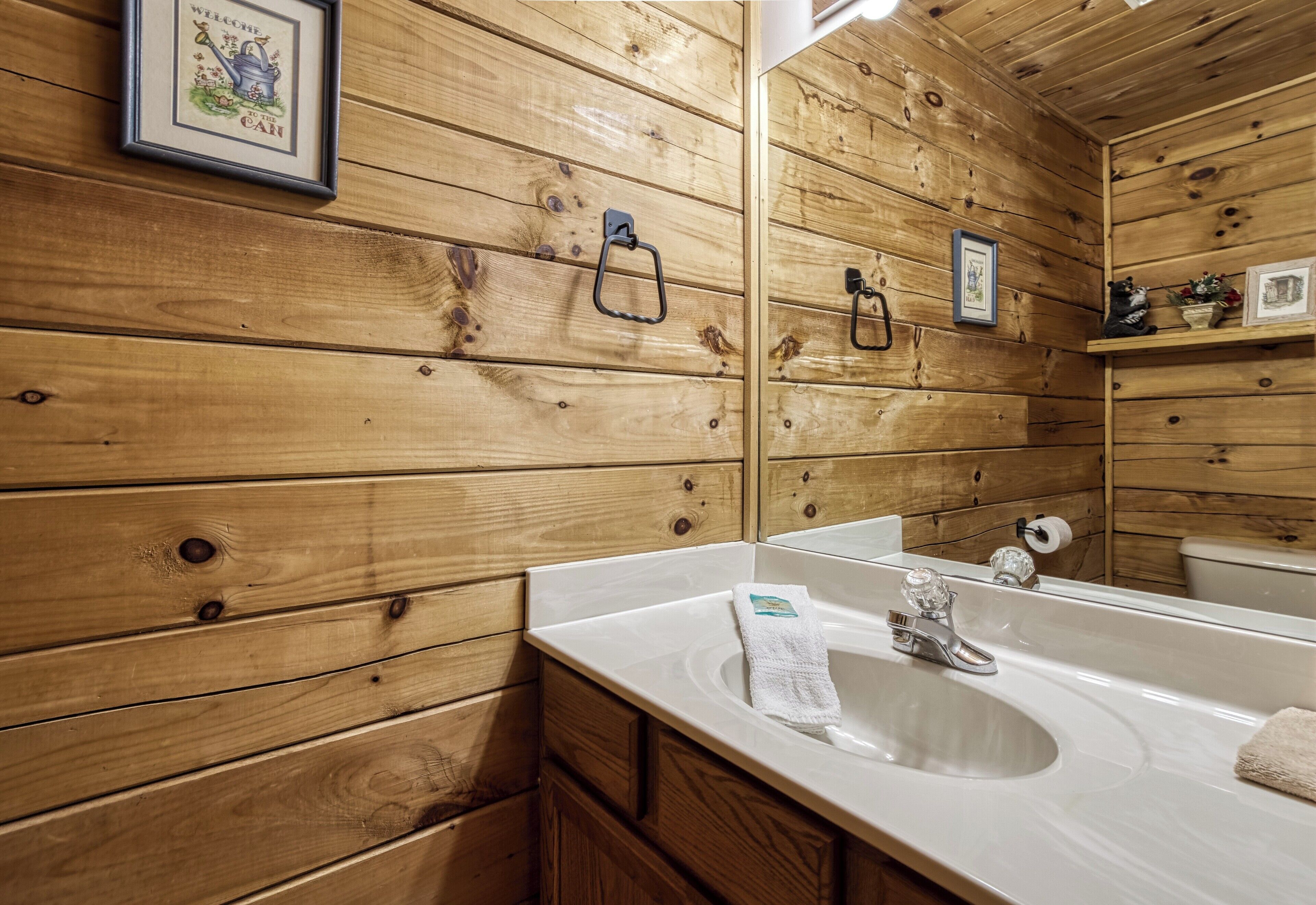 A wooden cabin-style bathroom with a large mirror, wooden walls, a sink, and a towel rack.