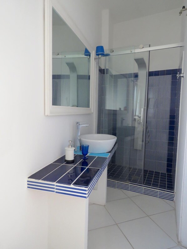 A bathroom with a white sink, blue-tiled countertop, and a glass shower enclosure.