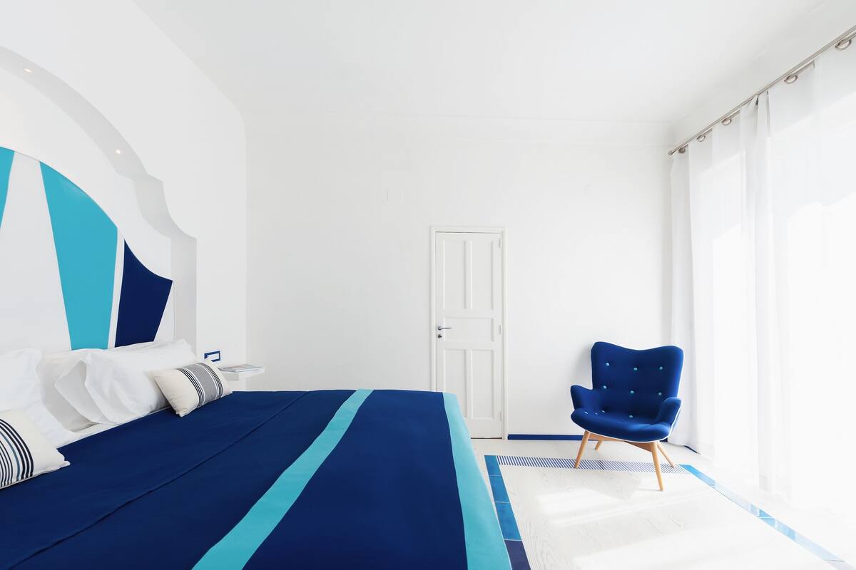 A modern bedroom with a large bed, a blue chair, and a white door.