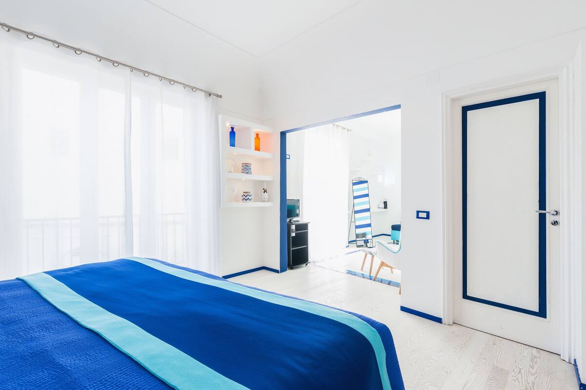 A hotel room with a bed, a wardrobe, a desk, and a bathroom visible through an open door.