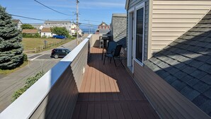 Un balcón con cubierta de madera, una mesa con sillas y vista a una calle y casas.