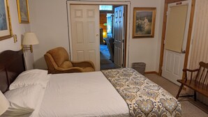 Una habitación de hotel con cama, una silla, una lámpara y una puerta que da a otra habitación.