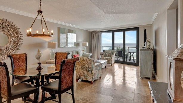 A spacious living area with a glass dining table surrounded by chairs, a chandelier, and a view of the ocean through large windows. - "Breathtaking Sunsets Await: Recently Renovated 4th-Floor Retreat in Beachside Two!" at Sandestin Golf and Beach Resort! (Miramar)