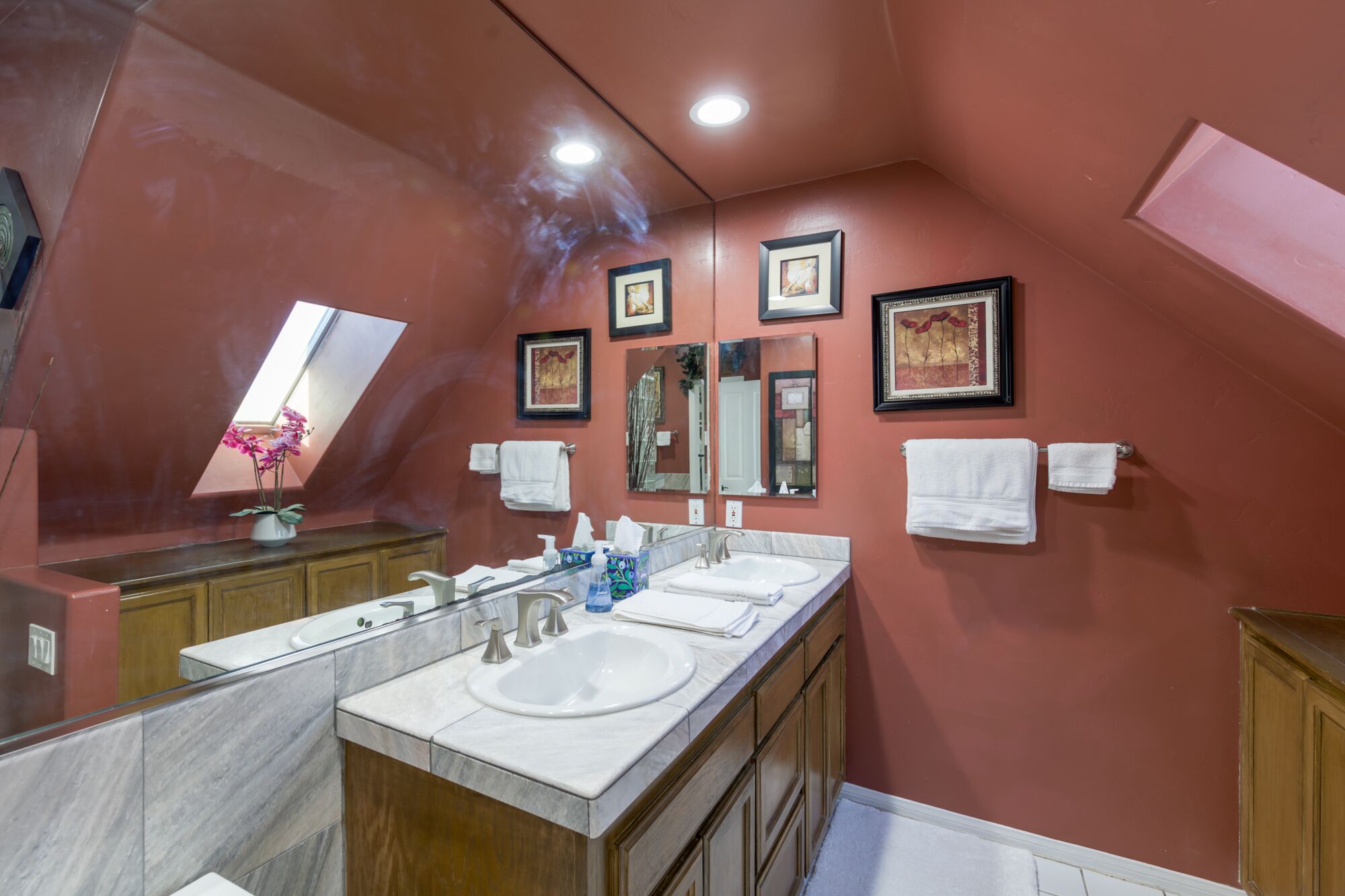 Un baño con dos lavamanos, un espejo grande y obras de arte enmarcadas en la pared.
