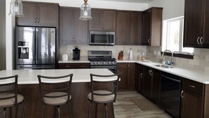 Een moderne keuken met donkerhouten kasten, roestvrijstalen apparatuur en een centraal eiland met barkrukken.