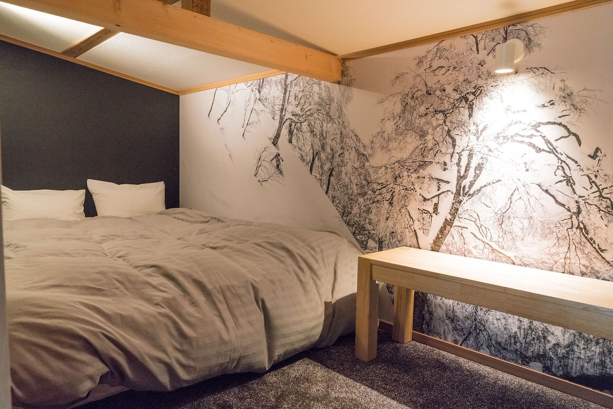 Un dormitorio con cama, un banco de madera y un mural de árboles en la pared.