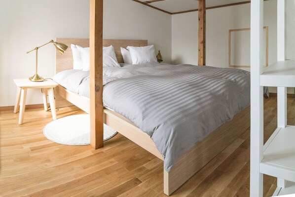 A neatly arranged bedroom with a wooden bed frame, a bedside table with a lamp, and a round rug on the wooden floor.