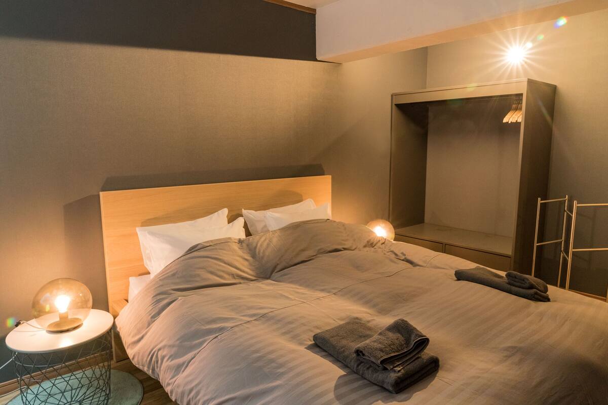 Una cama bien tendida con cabecera, una lámpara de noche y una toalla doblada sobre la cama.